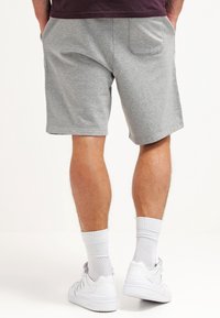 Shorts deportivos grises hechos de una tela suave, con un bolsillo trasero, combinados con zapatillas y calcetines blancos. Diseño simple y casual.