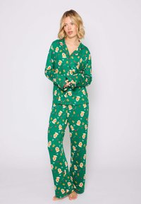 Ensemble de pyjama vert avec une coupe décontractée, comprenant des manches longues et un pantalon. Le matériau a une texture lisse et présente un motif ludique de bonhommes en pain d'épice et de cœurs.