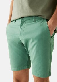 Shorts in cotone verde con una vestibilità su misura, dotati di tasche laterali, chiusura con bottone e una texture morbida.