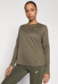 Αθλητική μπλούζα με μακριά μανίκια σε ελαιοπράσινο χρώμα, κατασκευασμένη από ύφασμα που απομακρύνει την υγρασία. Διαθέτει στρογγυλή λαιμόκοψη και μικρό λογότυπο στο στήθος.