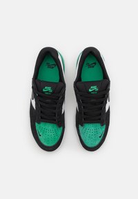 Nike SB cipők fekete velúrral, zöld kiegészítőkkel és fehér panelekben. Jellemzője a perforált orr, fekete cipőfűzők és zöld színű márkajelzéssel ellátott talpbetétek.
