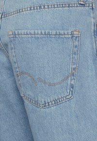 Ljusblå denimjeans med en bakficka som har ett böjt sömnadsmönster och kontrasterande oranga tråddetaljer.