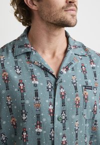 Green pajama shirt featuring a nutcracker and animal print, with snowflake accents, button closure, and a chest pocket labeled "JOCKEY."