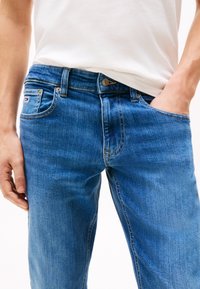 Niebieskie dżinsy z prostą nogawką, pięciokieszeniowym fasonem i delikatnym przecieraniem. Miedziane okucia i przeszycia kontrastują z tkaniną.