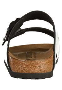 Svart och vit sandal med en korkfotbädd, justerbart rem, och platt gummisula. Designen har en slät yta och minimal detaljer.