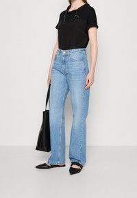 Top negro de manga corta con cuello ajustable, combinado con jeans de pierna ancha azul claro. Bailarinas negras de punta y un bolso tote negro.