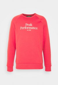 Rode sweatshirt met lange mouwen, ronde hals en geribde manchetten. Heeft witte tekst "Peak Performance" en "Est.1986" op de voorkant.
