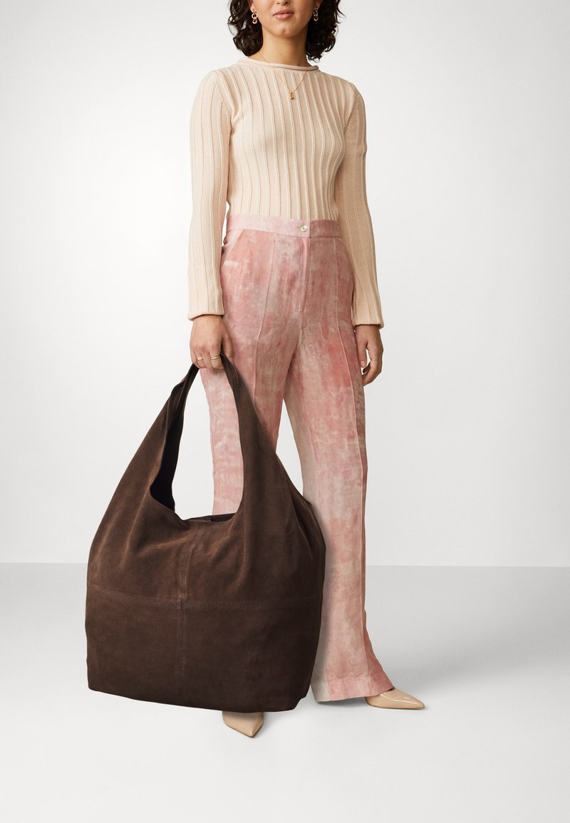 Braune Wildleder-Schultertasche mit einer lässigen Form, weiter Öffnung und nahtlosem Design. Die weiche Textur kontrastiert mit hellen Kleidungsstücken.