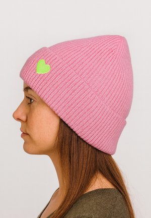 Pink ribbed knit beanie featuring a small green heart accent on the front. The beanie has a pointed top and is worn in a slouch style.