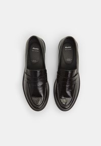 Zwarte leren loafers met een glanzende afwerking, voorzien van een dubbel bandontwerp en een eenvoudige, ronde neusvorm. Binnenin gemarkeerd met "Bata Echt Leer."