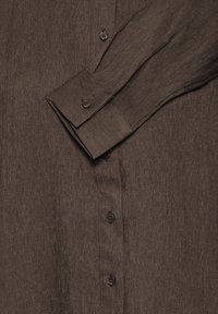 Braunes Langarmhemd mit geknöpften Manschetten und Knöpfen an der Vorderseite, das die Textur des Stoffes und die Nähdetails zeigt.