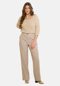 Bēša džemperis ar kamolu, V veida izgriezumu un trīs ceturtdaļu piedurknēm, kopā ar gaismas bēšām augsta vidukļa biksēm ar priekšpuses pogas aizdari.