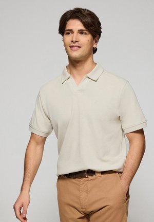 Beige poloshirt met een klassieke kraag en korte mouwen, gemaakt van zachte stof. Beschikt over een subtiele uitstraling op de borst en een relaxte pasvorm.