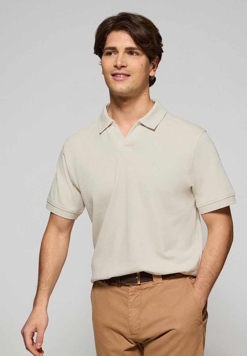 Polo beige con colletto classico e maniche corte, realizzato in tessuto morbido. Presenta un logo discreto sul petto e una vestibilità comoda.