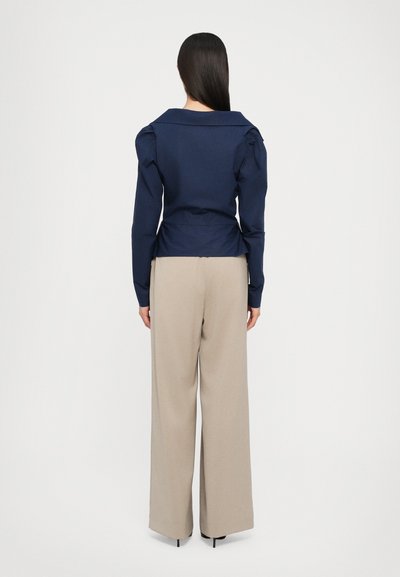 Navy long-sleeve top with puffed shoulders, collared neckline, and tailored fit, paired with beige wide-leg trousers. Smooth fabric texture.