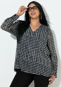 Sort-hvid mønstret bluse med V-hals og lange ærmer. Har et flydende design med gennemsigtigt stof og løs pasform.