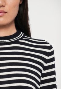 Maglione lavorato a maglia con strisce orizzontali blu navy e bianche, caratterizzato da un colletto rotondo a coste. Texture morbida, design slim fit.