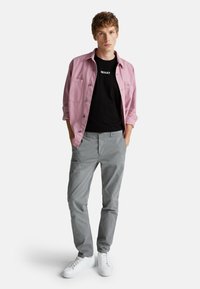 Camisa de botón rosa clara sobre una camiseta negra con el texto "WHAT", pantalones grises y zapatillas blancas. Estilo casual, textura suave y diseño simple.