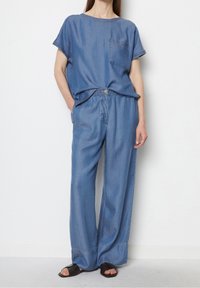 Jeansoutfit med en kortärmad topp med ficka och vida byxor. Båda är i en ljusblå nyans med synliga sömmar.