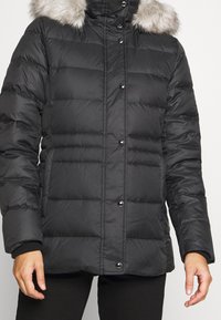 Chaqueta de plumas negra con un cuello alto, con un ribete de pelo sintético desmontable, diseño acolchado y botones a presión negros en el frente.