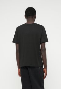 Μαύρο κοντομάνικο βαμβακερό μπλουζάκι με στρογγυλή λαιμόκοψη, ίσια τελείωμα και λεία υφή, από την πίσω πλευρά.