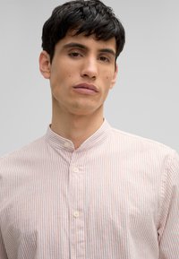 Camicia a righe con collo alla mandarino, righe rosa chiaro e bianche, tessuto morbido e chiusura con bottoni nella parte anteriore.