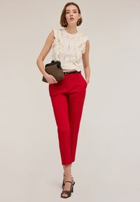 Blusa bianca con volant e dettagli in pizzo, abbinata a pantaloni rossi su misura. Accessoriata con una pochette testurizzata e sandali neri con cinturino alla caviglia.