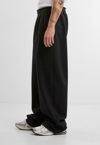 Melnas sporta bikses ar brīvu piegriezumu un elastīgu jostu, saskaņotas ar metalizētām sporta apaviem. Gluda tekstūra un bez redzamām rakstiem vai rotājumiem.