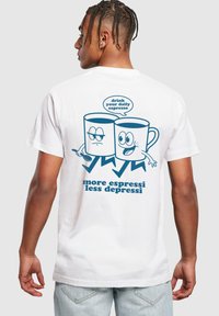 Balta medvilninė marškinėlių su mėlyna grafika, kurioje pavaizduoti du puodeliai su veidais, tekstas "gerk savo kasdienį espresso" ir "daugiau espresso, mažiau depresijos."