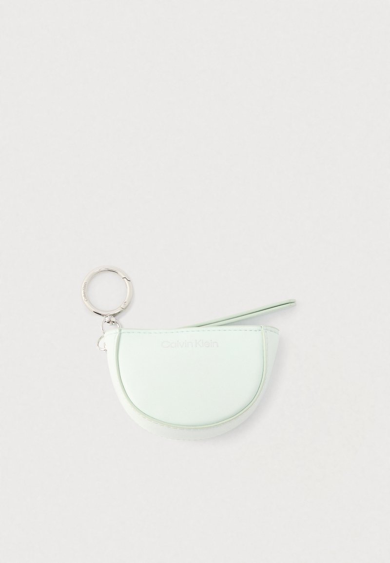 Μικρό πορτοφολάκι σε παστέλ πράσινο χρώμα σε σχήμα ημισελήνου με φερμουάρ και ασημένιο μπρελόκ Calvin Klein, πάνω σε απλό λευκό φόντο.