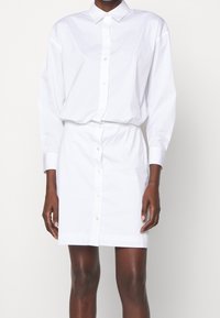 Vestito bianco in cotone, con bottoni frontali, maniche lunghe e una vestibilità rilassata con vita elastica.