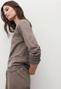 Top marrone a maniche lunghe in tessuto morbido con polsini arrotolati e cuciture laterali, abbinato a pantaloni con vita elastica coordinati. Design semplice e aderente.