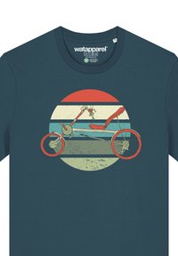 Türkises Baumwoll-T-Shirt mit einer Retro-Grafik eines Dreirads vor einem kreisförmigen gestreiften Hintergrund in Rot-, Blau- und Creme-Tönen.