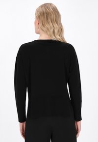 Schwarzer oversized Pullover mit geripptem Saum, langen Ärmeln und rundem Halsausschnitt, der eine glatte Textur und eine lockere Passform aufweist.