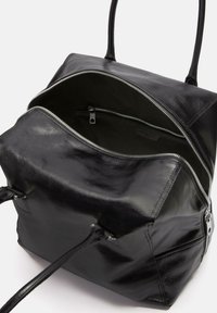 Sac à main en cuir noir avec une forme structurée, comportant deux poignées, des fermetures éclair en argent et une poche intérieure zippée. Texture lisse sur l'ensemble.