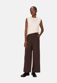 Haut en tricot sans manches beige clair associé à un pantalon large marron et des chaussures noires. La tenue présente une coupe décontractée et un design simple.