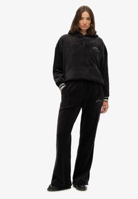 Zwarte velours hoodie en bijpassende broek set, met een ontspannen pasvorm, voorzak, streepaccenten op de mouwen en geborduurd logo-detail.