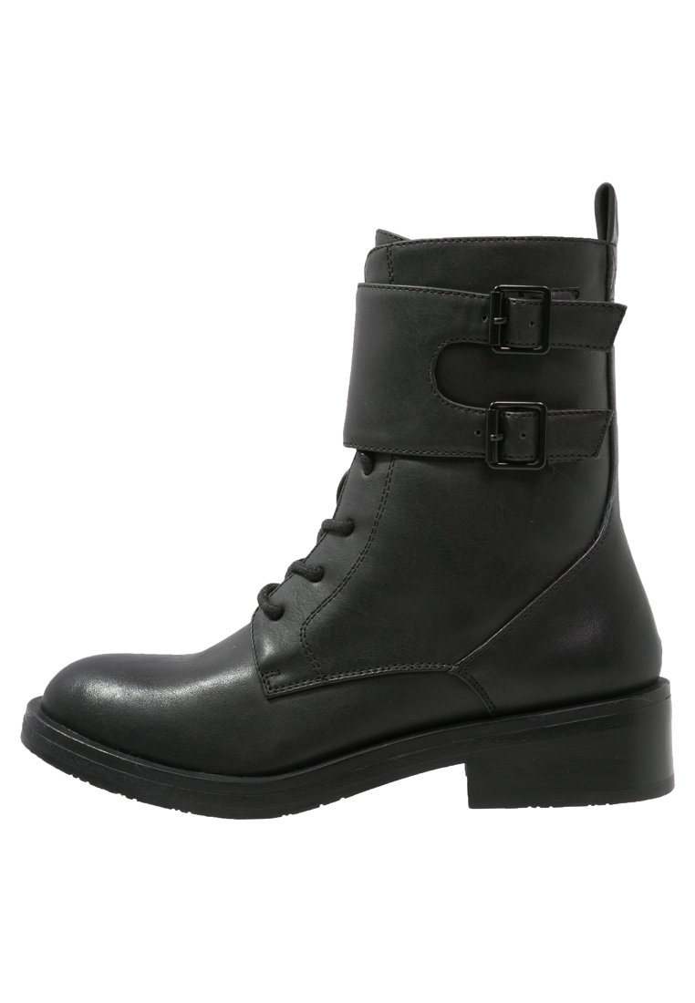 Botín de cuero negro hasta el tobillo con cordones, dos correas con hebillas, punta redondeada y un tacón grueso. Textura suave y diseño resistente.