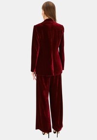 Bordowy aksamitny garnitur składający się z marynarki i spodni o szerokich nogawkach, z gładką fakturą i dopasowanym krojem, pokazany od tyłu.