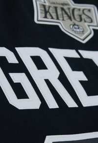 Detail eines Los Angeles Kings Trikots mit dem Namen "GRETZKY" in weißen gestickten Buchstaben auf einem schwarzen Stoffhintergrund, versehen mit einem Logo-Patch.