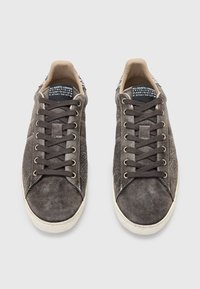 Grå ruskinds sneakers med et struktureret design, rund tå, kontrastfyldt hvid gummisål og flade snørebånd. Har et trykt mærke indeni.