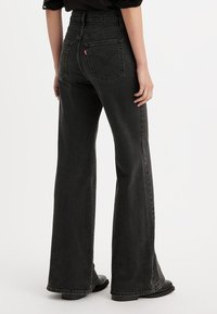 Høytlivete svarte fakkeljeans laget av denim, med baklommer, subtil søm og en avslappet passform med vid benåpning.