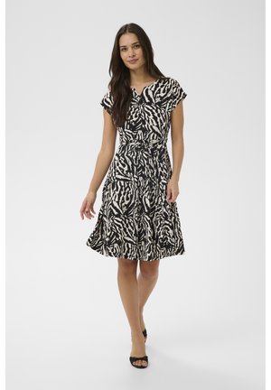 Naine kõnnib edasi, kandes põlvepikkust must-valget sebratrükiga kleiti, millel on lühikesed varrukad, ning musti avatud varbaga kontsakingi.