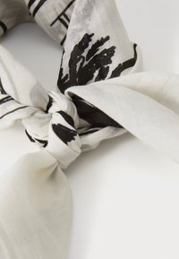 Eșarfă albă și neagră cu un design legat. Prezintă un model floral și dungi pe un material moale și ușor, evidențiind detaliile texturale.