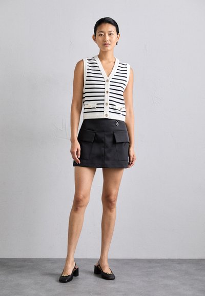 Ράστα μανικιών αμάνικου γιλέκου σε ναυτικό μπλε και λευκό με κουμπιά, συνδυασμένο με μια μαύρη μίνι φούστα που διαθέτει δύο μπροστινές τσέπες. Μαύρες ψηλές μπαλαρίνες.