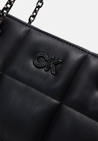 Black leather handbag with quilted texture, featuring a prominent CK logo, and a chain strap for carrying.