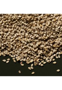 Sesamfrön spridda på en mörk yta; runda, små och beige med en lätt glänsande yta och ojämn fördelning.