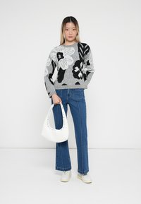 Maglione grigio lavorato a maglia con motivo floreale in bianco e nero, abbinato a jeans blu a vita alta e a una borsa bianca con borchie. Le sneakers bianche completano il look.