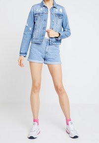 Ljusblå denimjacka med slitna detaljer, i kombination med ljusblå shorts. Vit T-shirt under, rosa strumpor och vita sneakers.