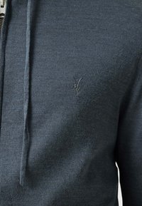 Felpa grigia scura con zip realizzata in morbido tessuto a maglia; dotata di cappuccio con cordino e di un logo ricamato discreto sul petto.